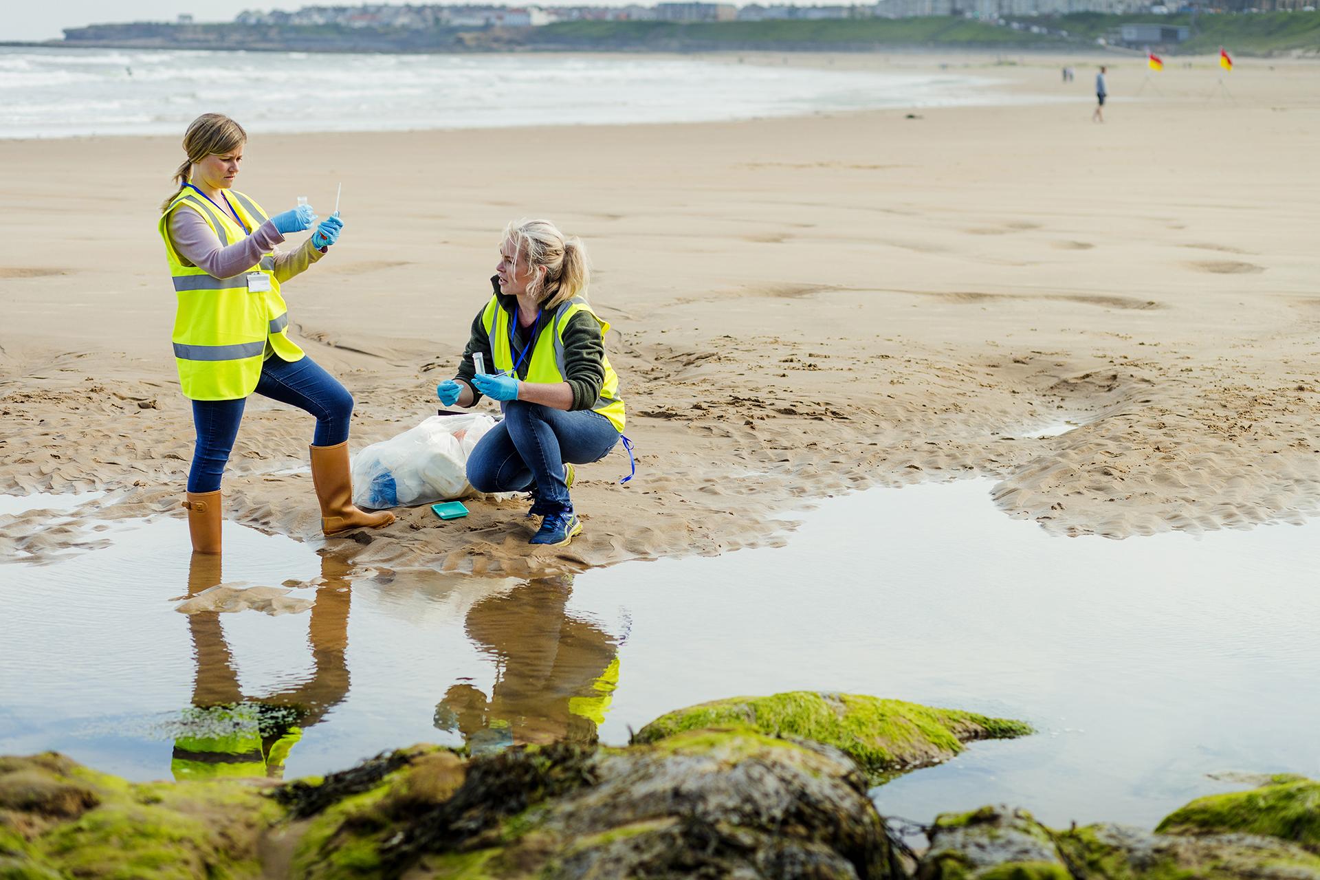 Two women wearing protective gear testing water on a beach